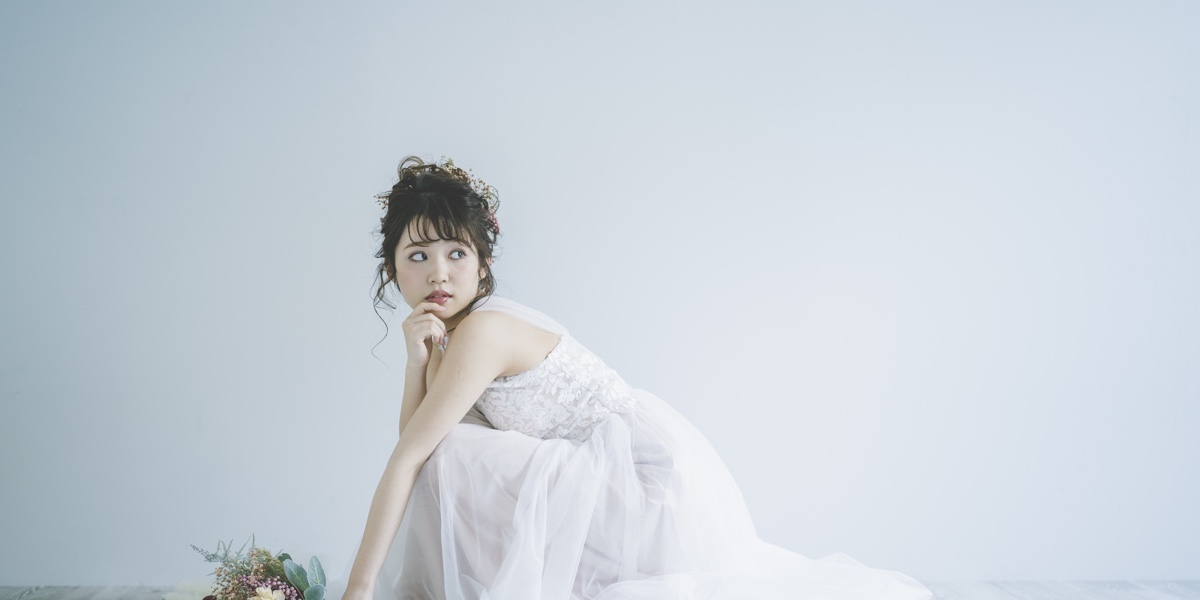 白い空間で、花束をそばに置いて座るウェディングドレス姿の花嫁