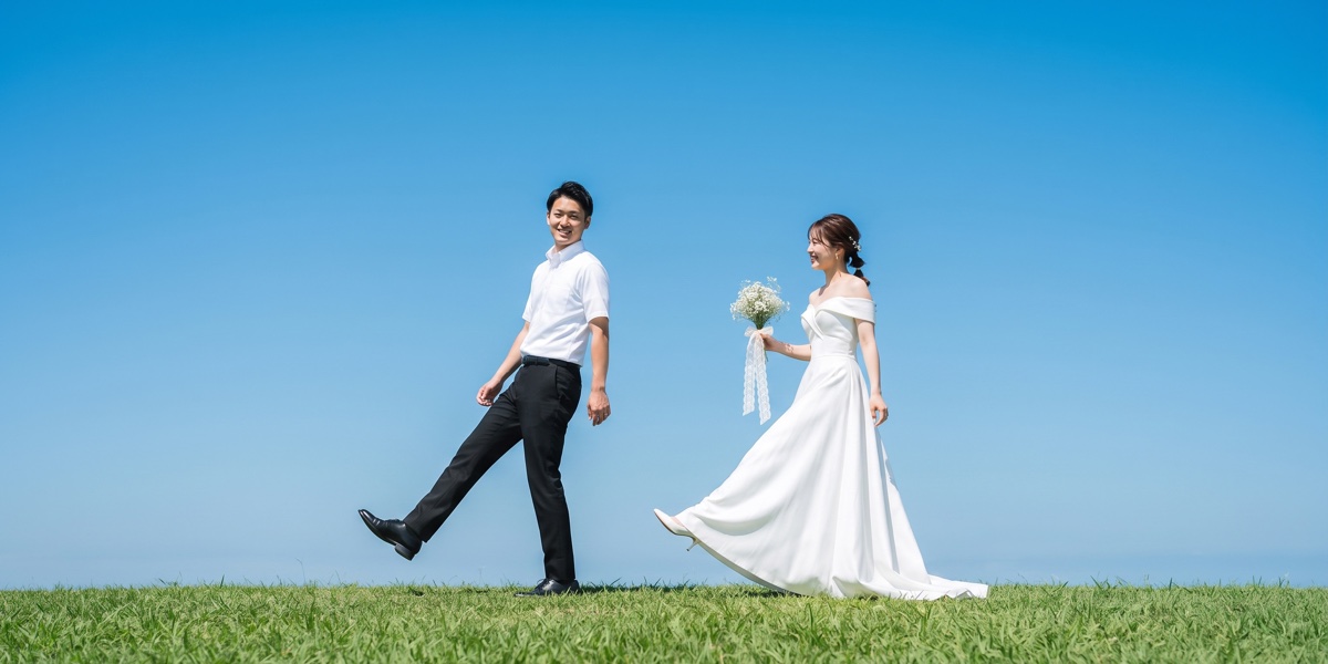 青空の下、芝生の丘を並んで歩く新郎新婦
