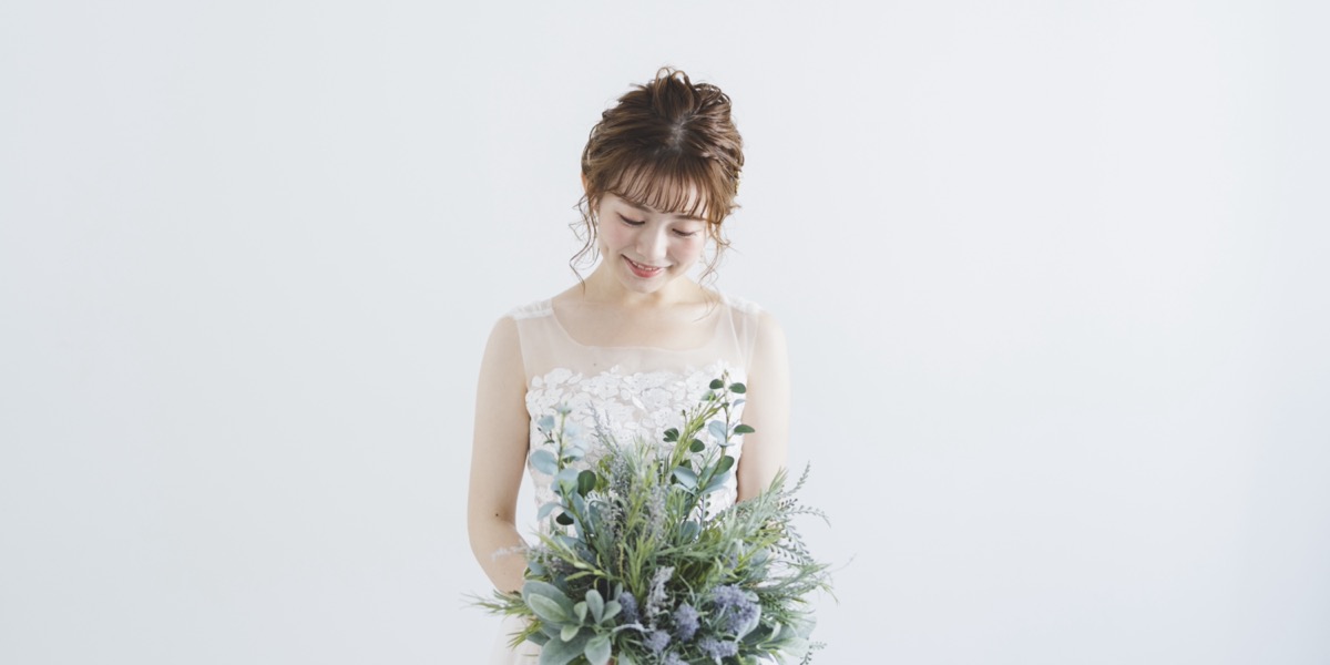 白い背景で、グリーンのブーケを持って微笑む花嫁